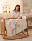 Stork And Baby Pink Rainbow starter pack with babygrow, bodysuit, hat, mittens, and blankie in a crib with a mother and baby.