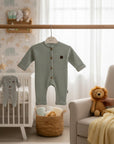 Stork And Baby sage green raised waffle knit romper with wooden buttons and a small brown patch detail.