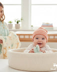 Stork And Baby orange and white striped knit baby hat. Happy baby sitting in a basket.