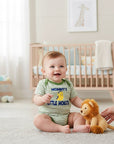 Stork And Baby green and white striped baby romper with 'Mommy's Little Monster' graphic. Baby sitting on rug.