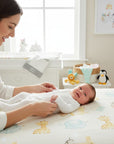 Stork And Baby white long-sleeve babygrow with snap closures, worn by a baby lying on a giraffe-print blanket.