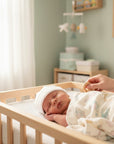 Stork And Baby white 100% cotton beanie on a sleeping infant in a crib. Soft and breathable.