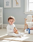 Stork And Baby white 100% cotton long sleeve baby set with navy polka dot trim. Baby sits on rug holding giraffe toy.