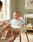 Stork And Baby white toweling dribble bibs with scalloped edge, worn by a baby in a high chair.
